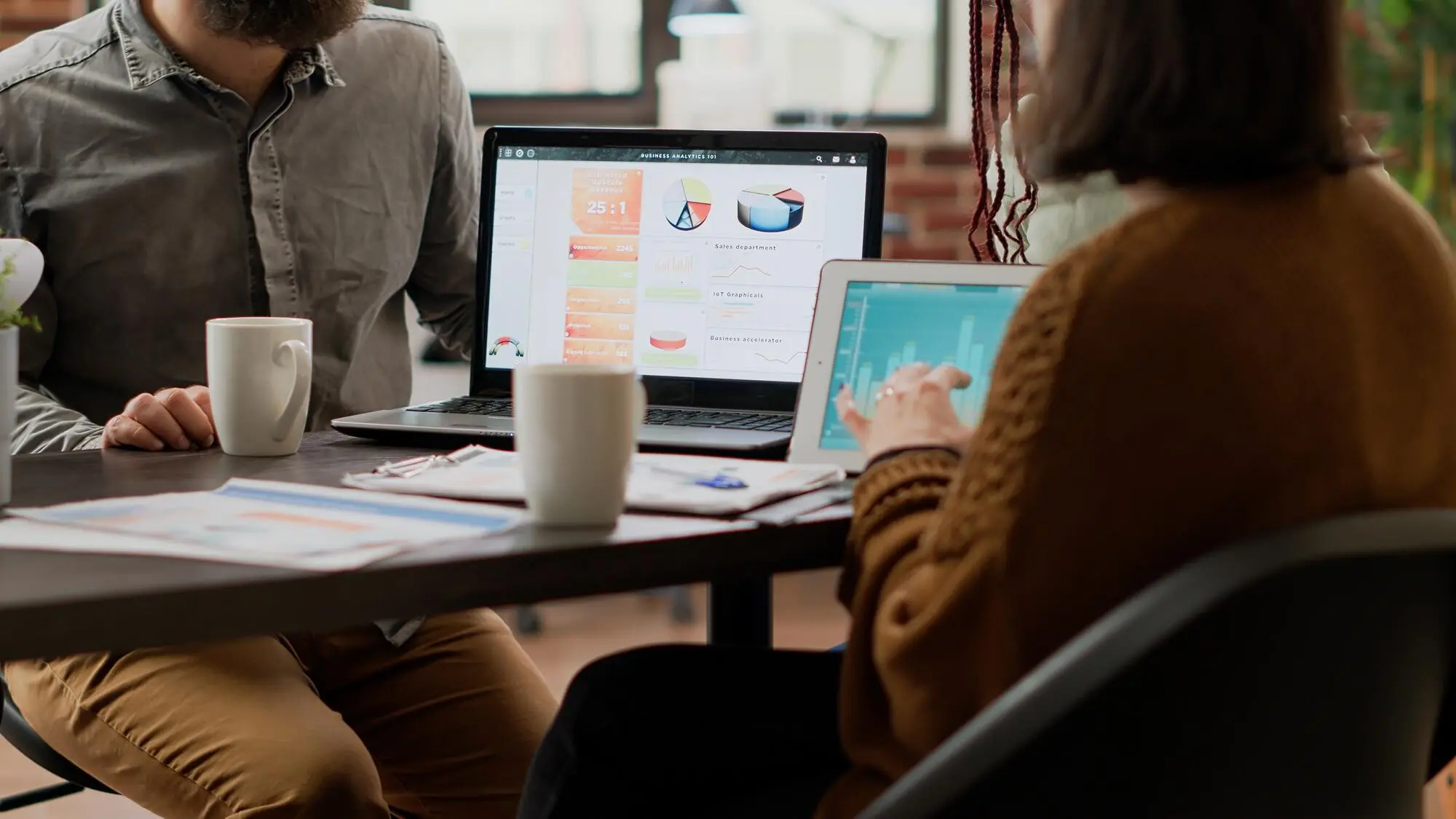 Eine multiethnische Gruppe von Kollegen arbeitet mit einem digitalen Tablet an der Analyse von Diagrammen und nutzt Informationen aus Online-Recherchen, um einen Infografikbericht zu erstellen. Personen analysieren Diagramme im Sitzungssaal.